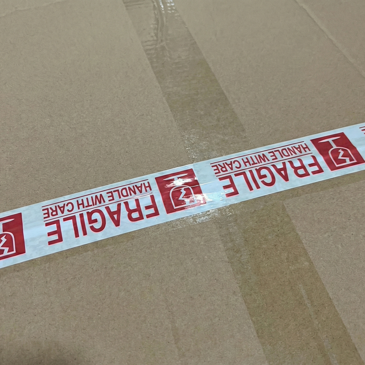 Cardboard box sealed with adhesive tape printed with the text "Fragile" in red to identify delicate merchandise.