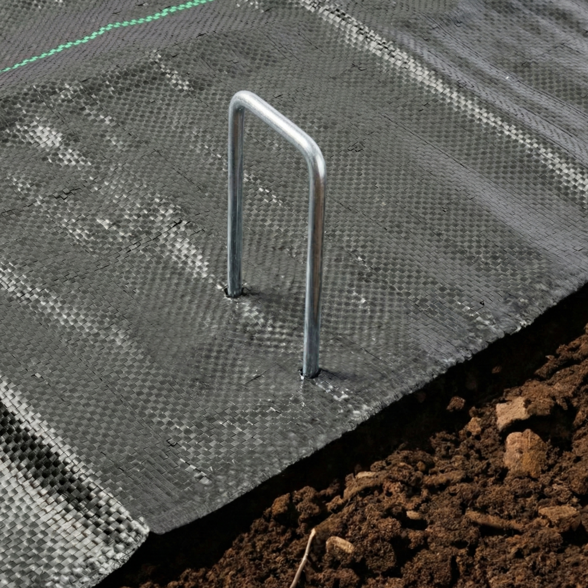 Installation of anti-weed mesh or ground cover using high-strength metal staples for landscaping in Santo Domingo.