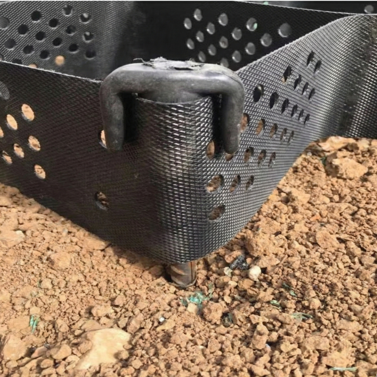Capuchon d'ancrage fixant une géocellule noire sur un terrain en terre pour la stabilisation des talus en République dominicaine.