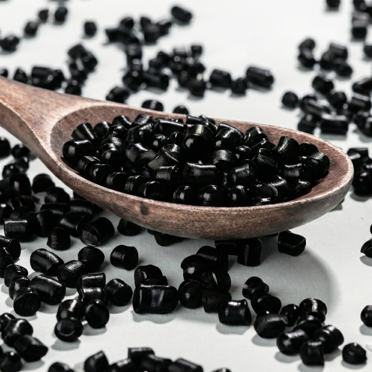 Spoon showing black polyethylene pellets or masterbatch, virgin plastic raw material granules used in the industry for manufacturing black stretch film.