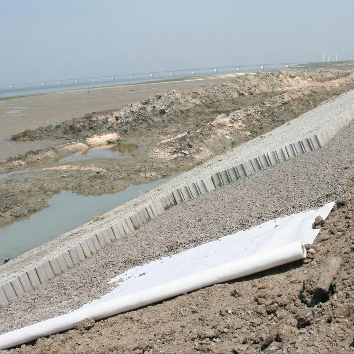 Geotextil no tejido de poliéster (PET) blanco aplicado en obra para separación de capas de suelo y refuerzo de drenaje.