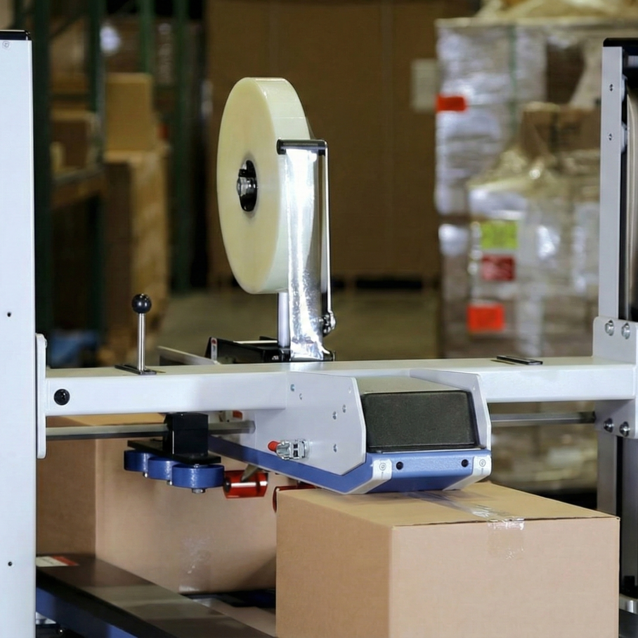 Close-up of the head of an automatic taping machine applying adhesive tape to a box on a production line.