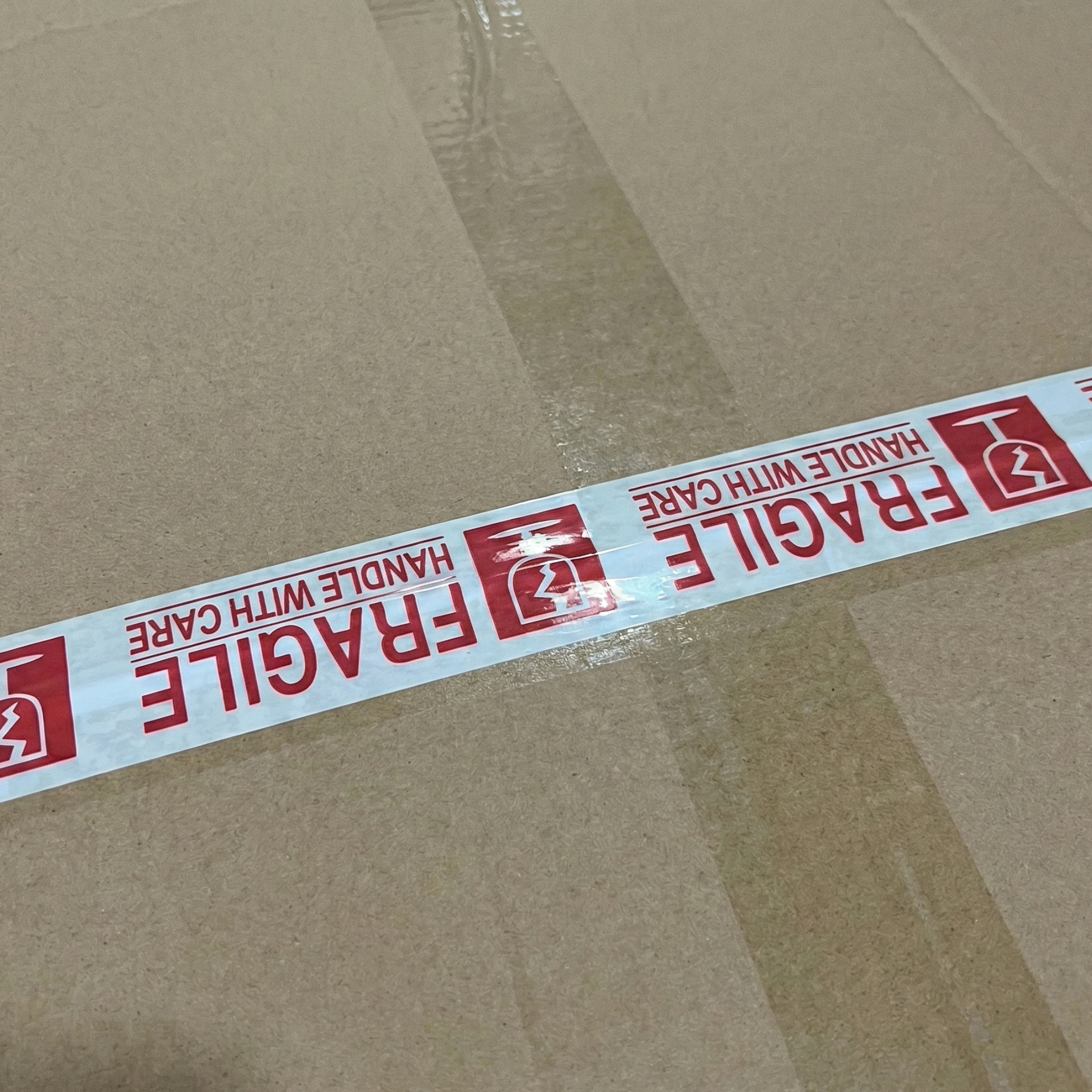 Caja de cartón sellada con cinta adhesiva (teipe) impresa con el texto "Fragile" (Frágil) en rojo para identificar mercancía delicada.
