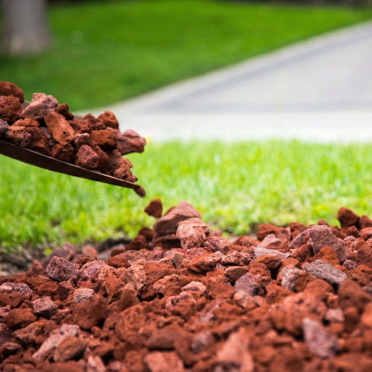 Outil de jardinage versant du gravier volcanique rouge sur le sol à côté du gazon pour la décoration de jardins en République dominicaine.