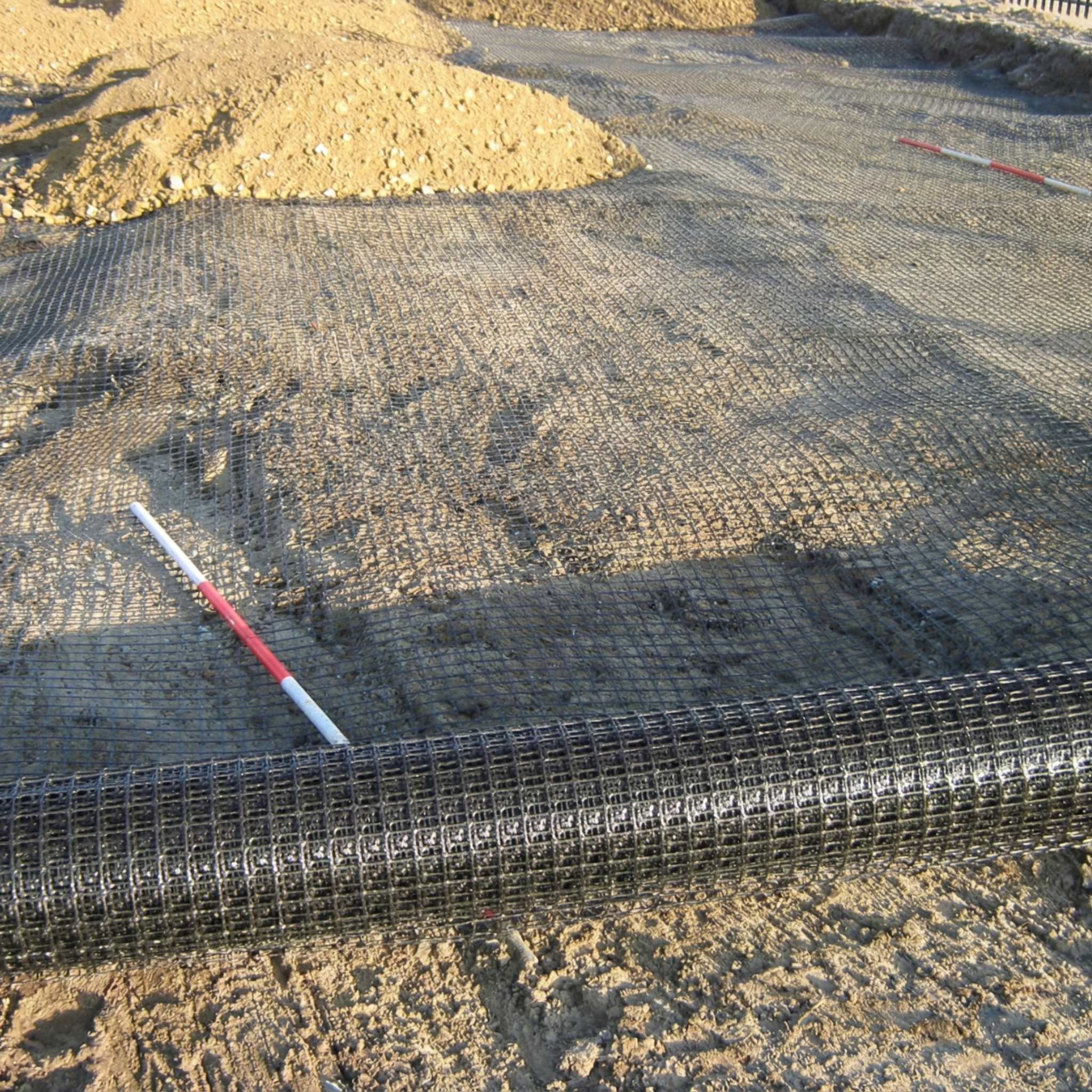 Despliegue de geomalla biaxial negra sobre el terreno para el refuerzo de bases granulares en obras civiles de Santiago, RD.