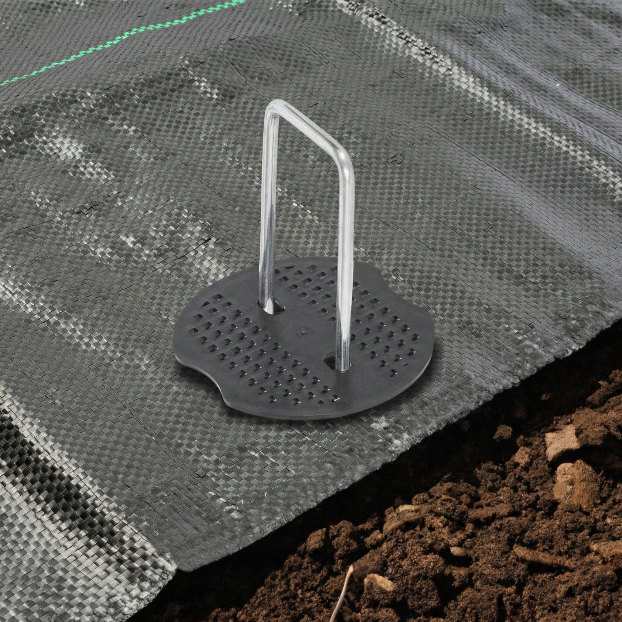 U-shaped fastening staple with a plastic retention disc securing anti-weed mesh in gardening projects in the Dominican Republic.