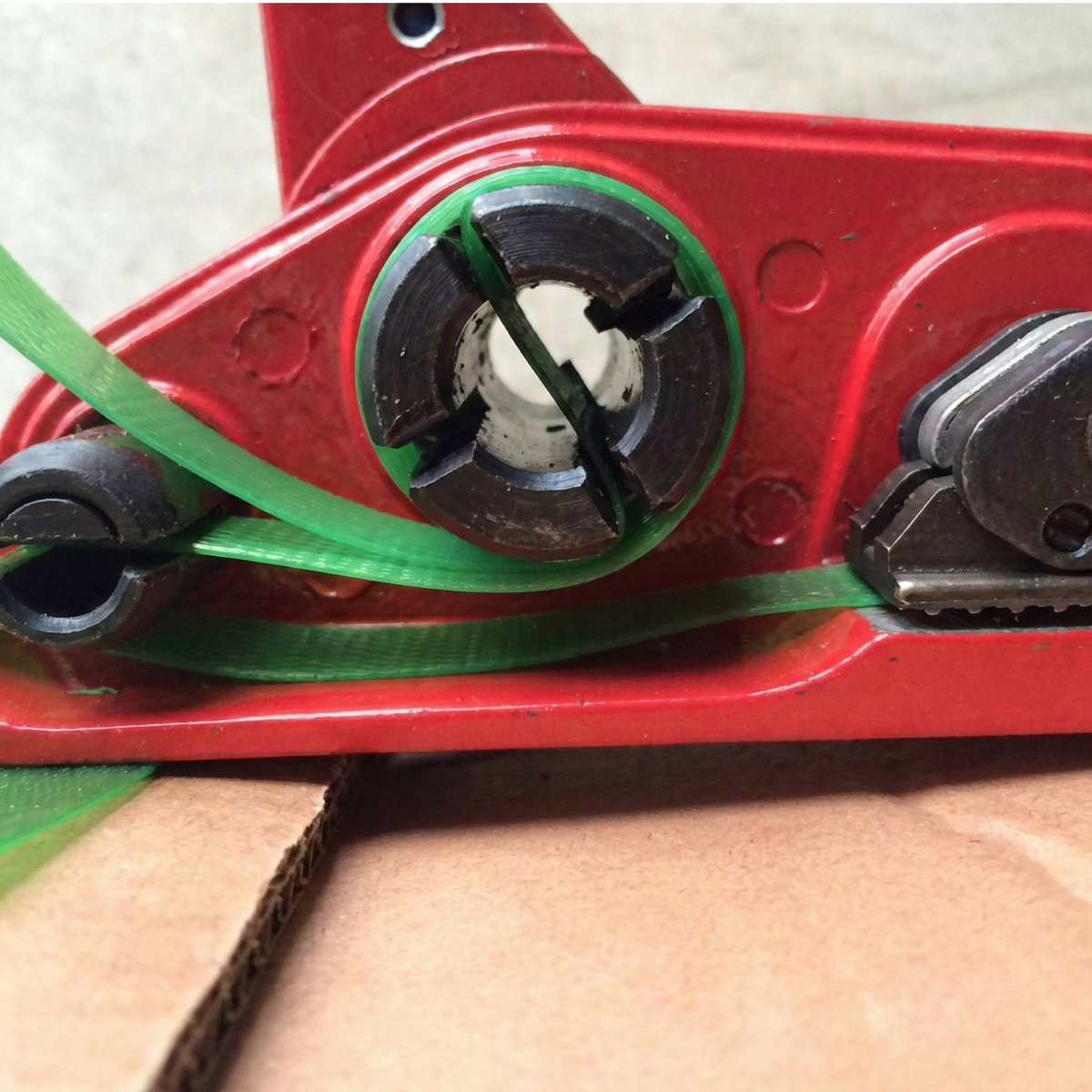 Close-up of green PET strap being adjusted by an industrial manual tensioner.